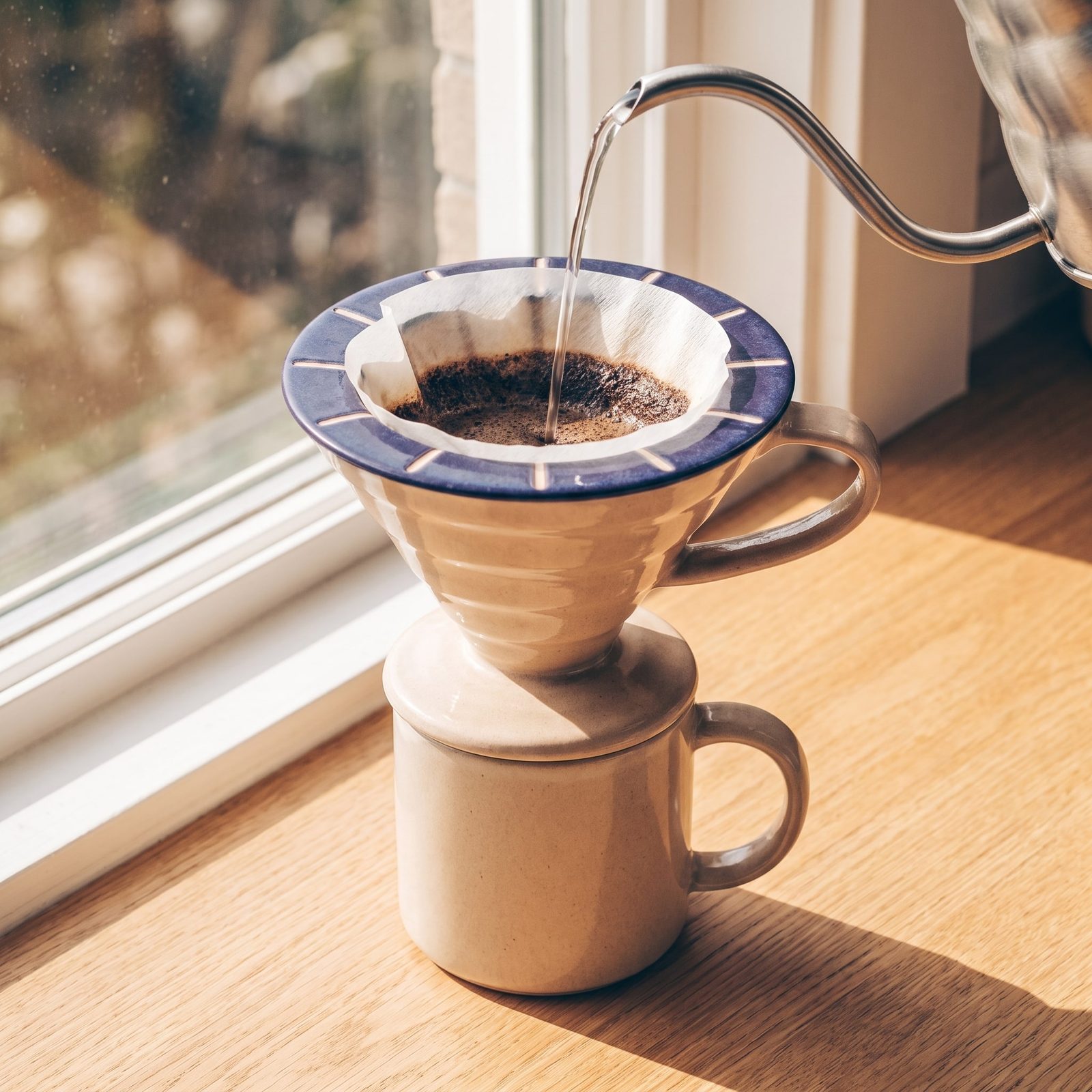 Concept sample: ceramic pour-over dripper with a deep indigo rim on a mug by a sunny window, as water is poured from a gooseneck kettle